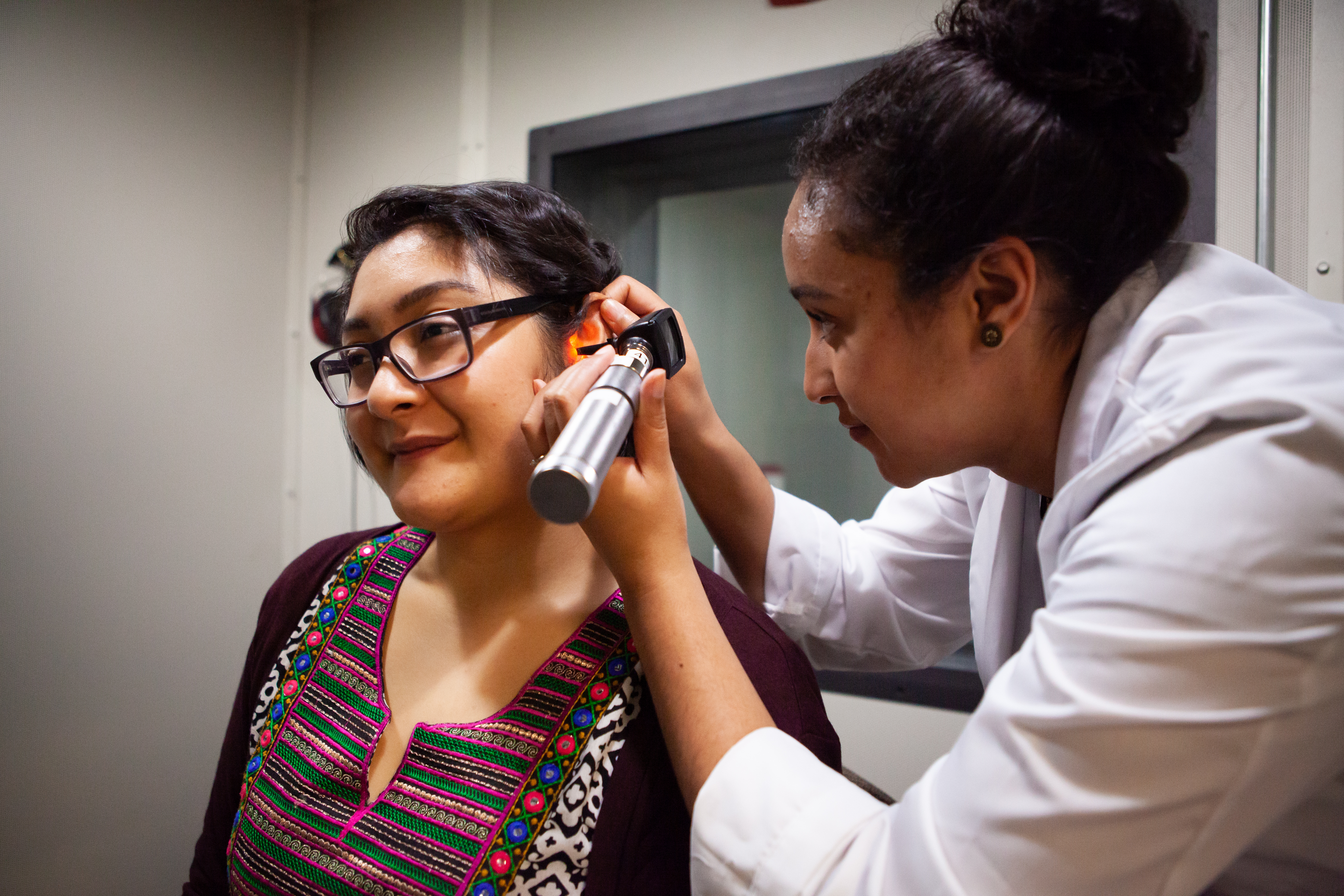 An audiology student uses an otoscope to examine a patient's ear canal.