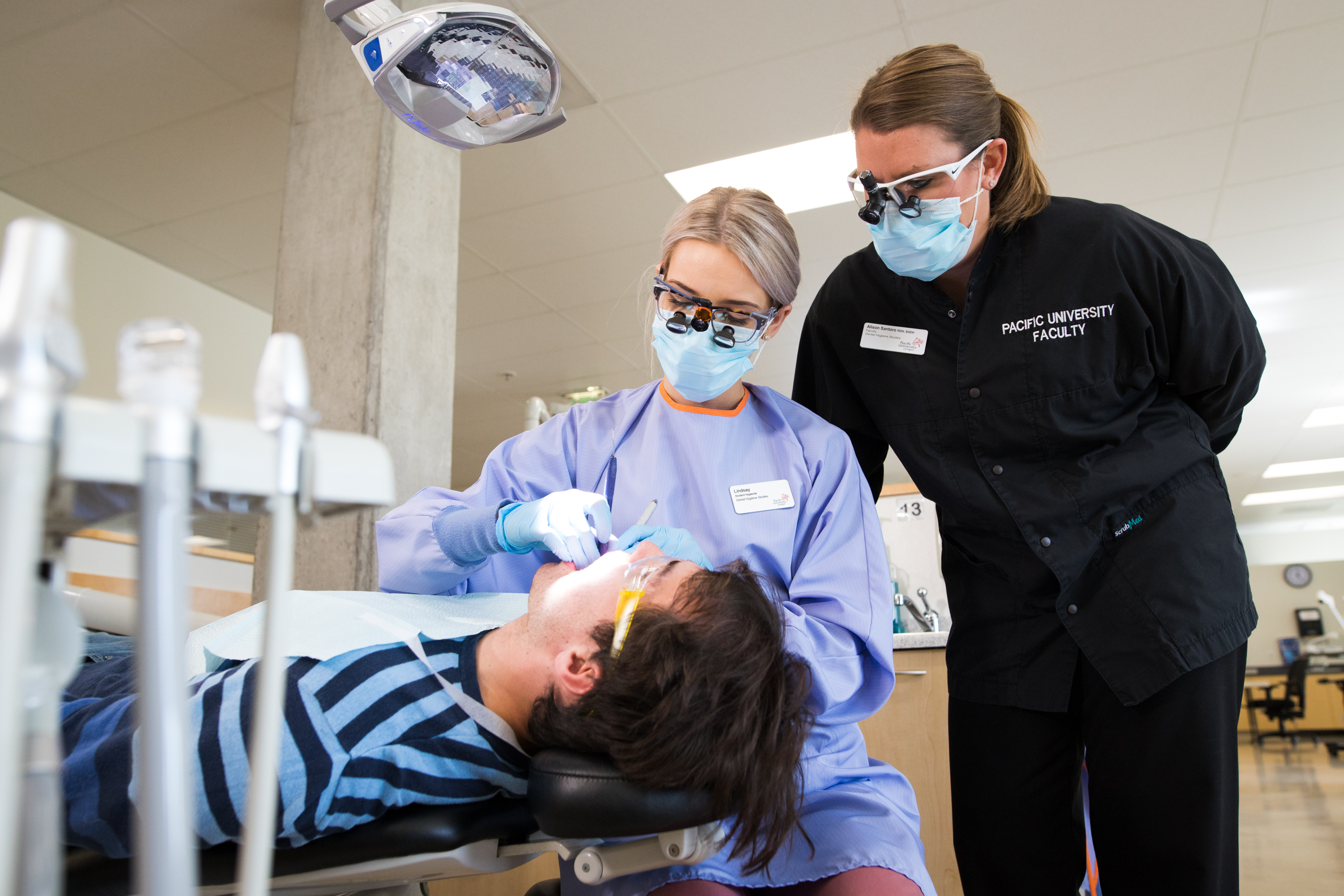 A dental hygiene students cleans a patient's teeth under the supervision of a faculty member.