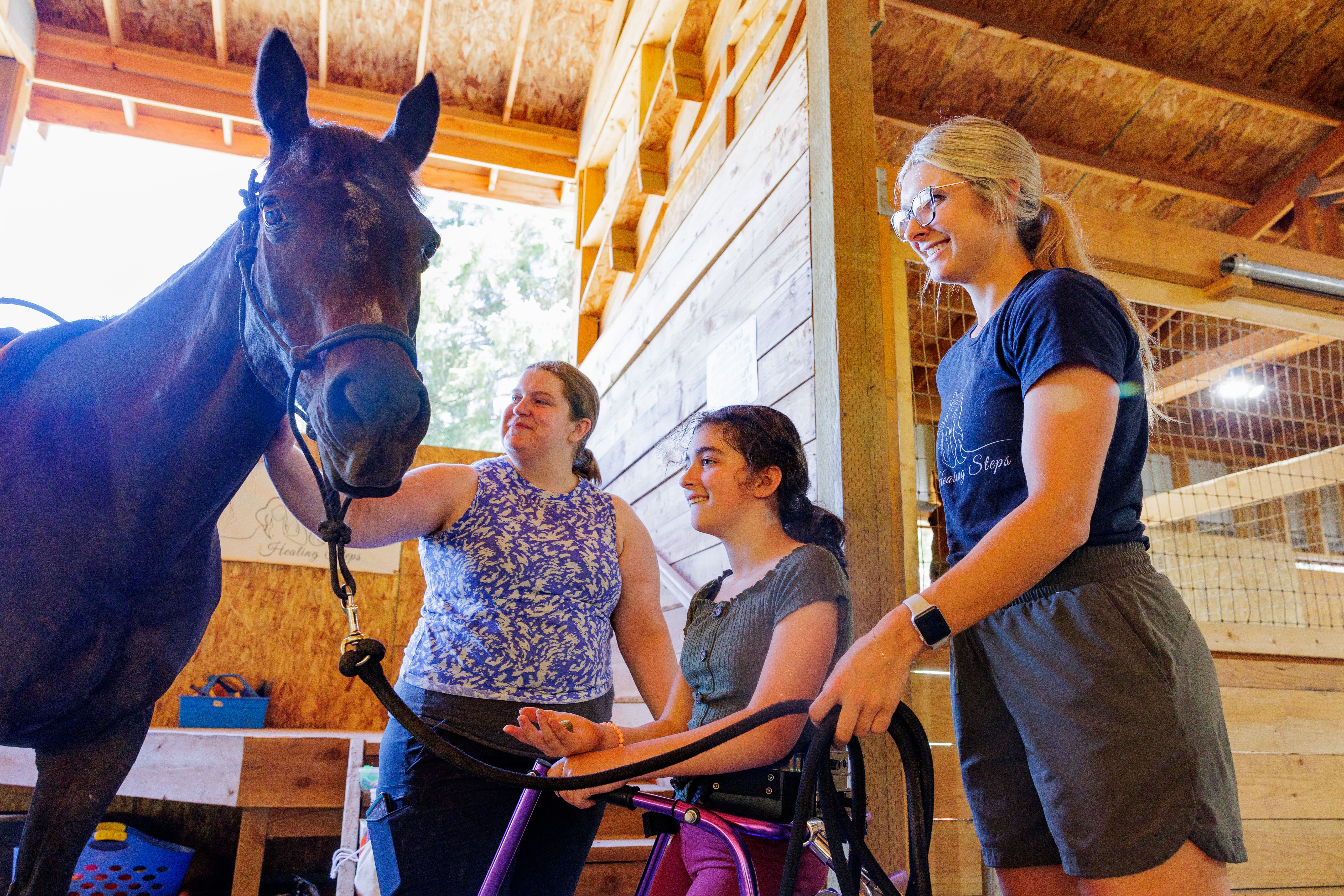 A child participates in equine therapy with two Pacific occupational therapy students.