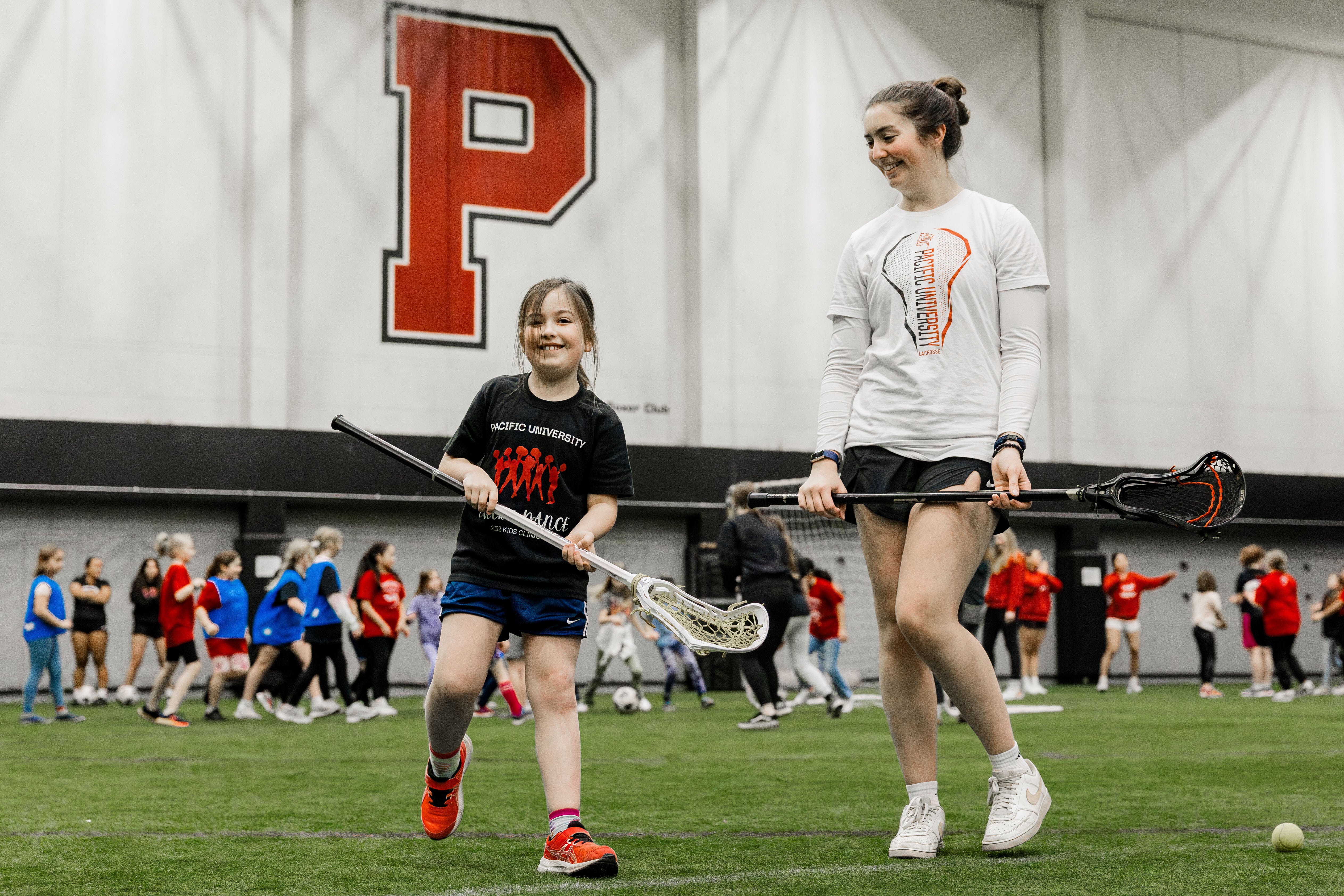 A woman teaches a young girl how to use a Lacrosse stick during the women and girls in sports event at Pacific's Stoller Center.