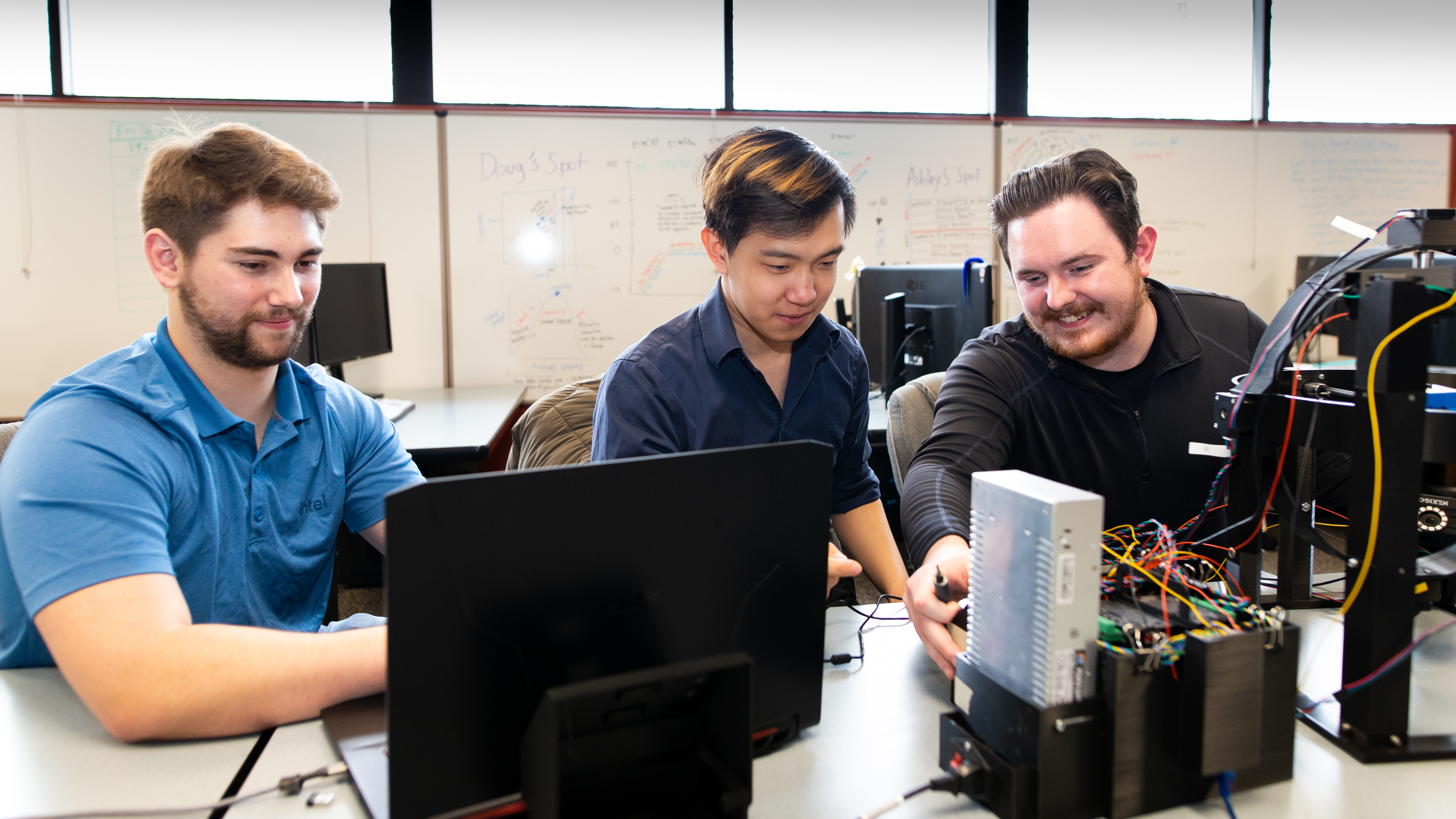 Three computer science students work on a small robot that can solve puzzles.