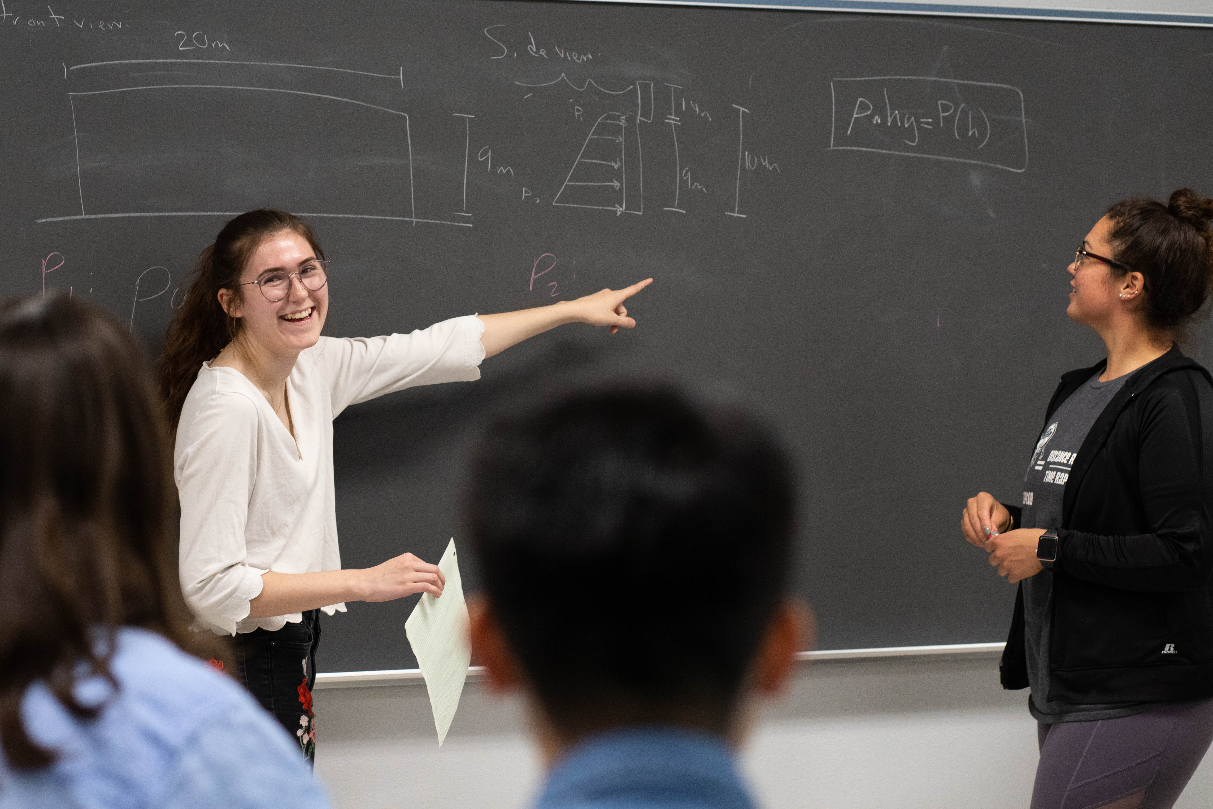 A Pacific undergraduate student works through a physics problem at a blackboard.