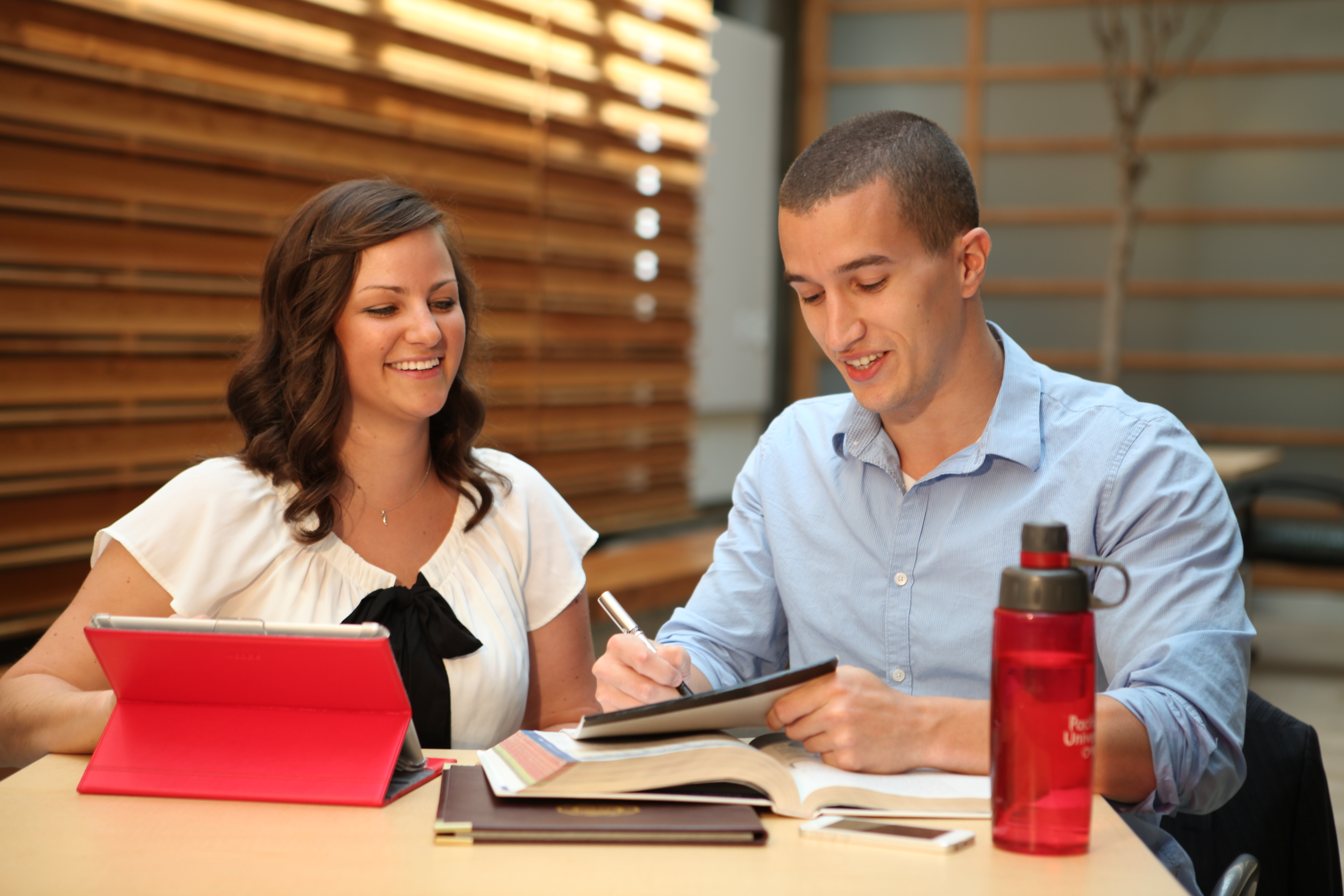 Two students sit at a table studying over an open textbook.