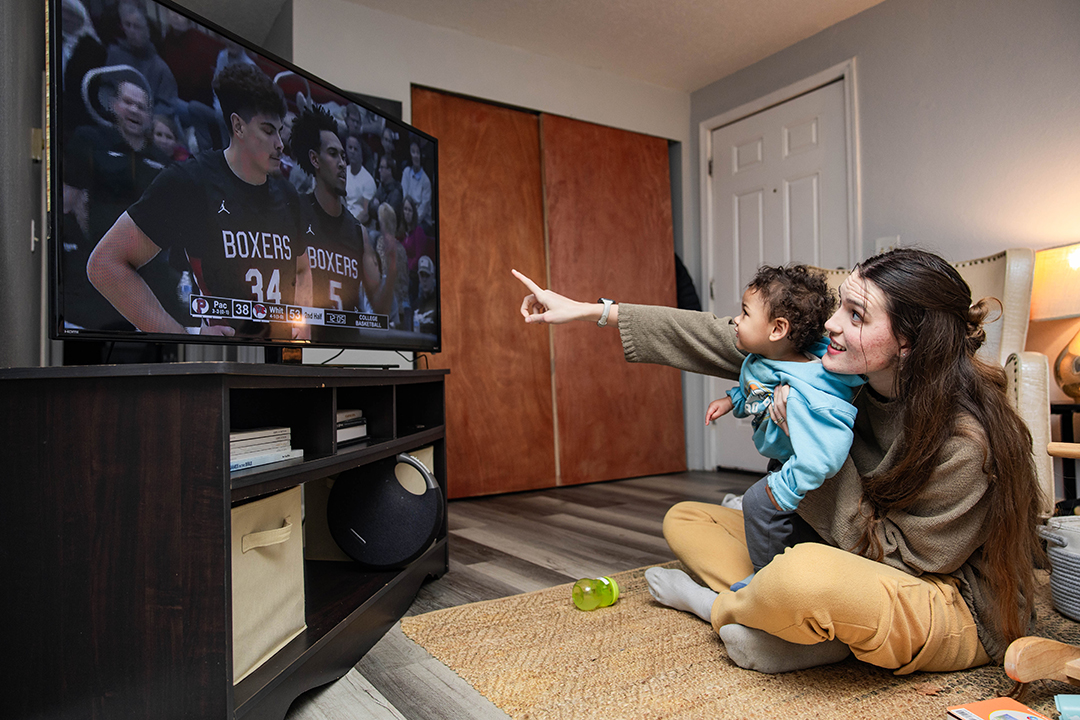 Kristin and Rocket watch on TV as Devin Fortune '25 and the Pacific University Boxers play at Whitworth