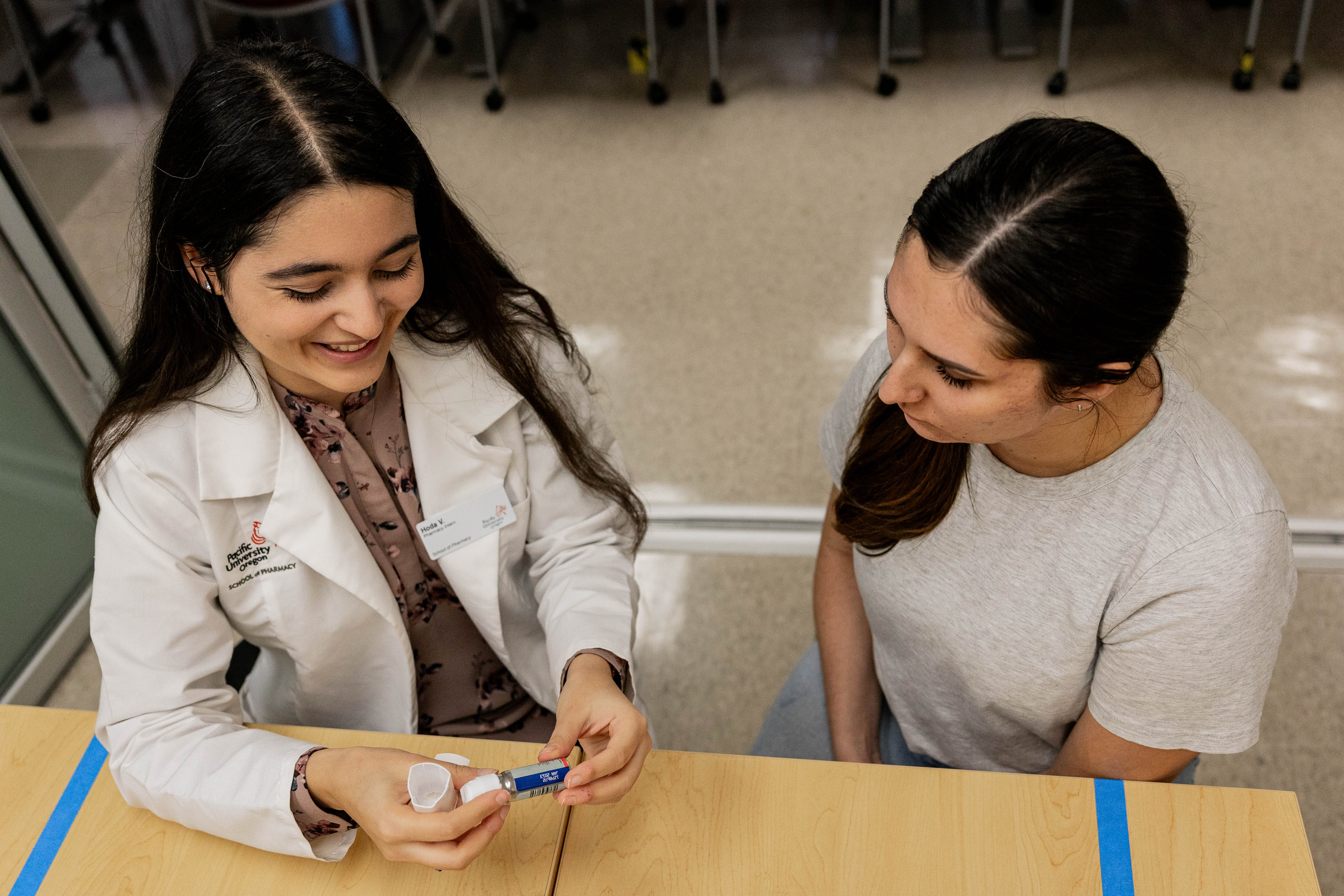 Two Pacific pharmacy students demonstrate how to explain medication instructions to patients.