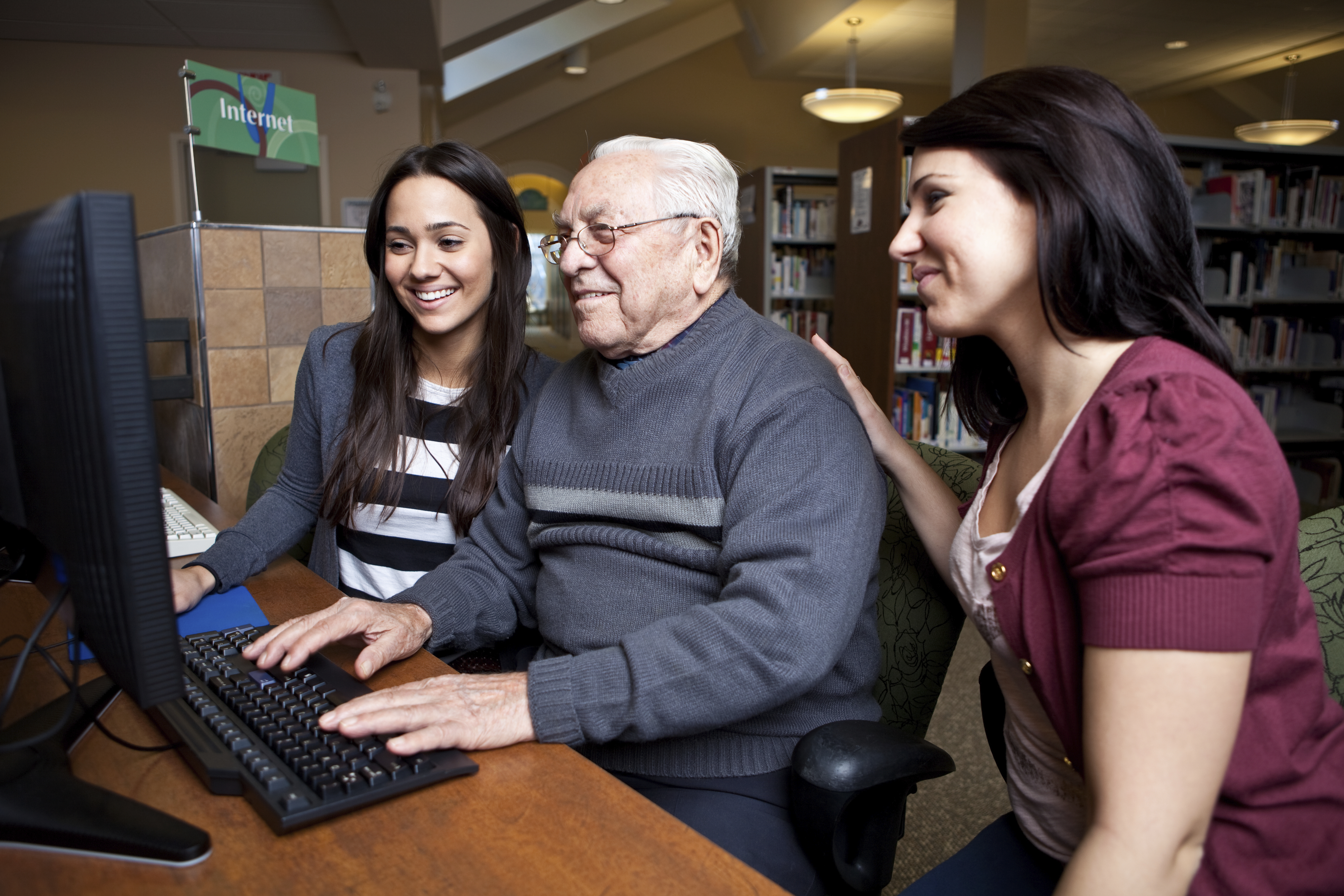 Two social work students help an elderly man use a computer.