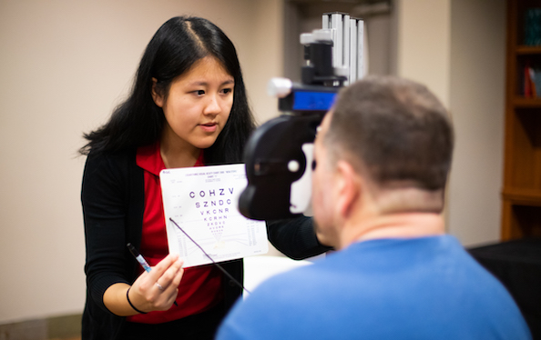 Optometry student holds up exam sheet for patient