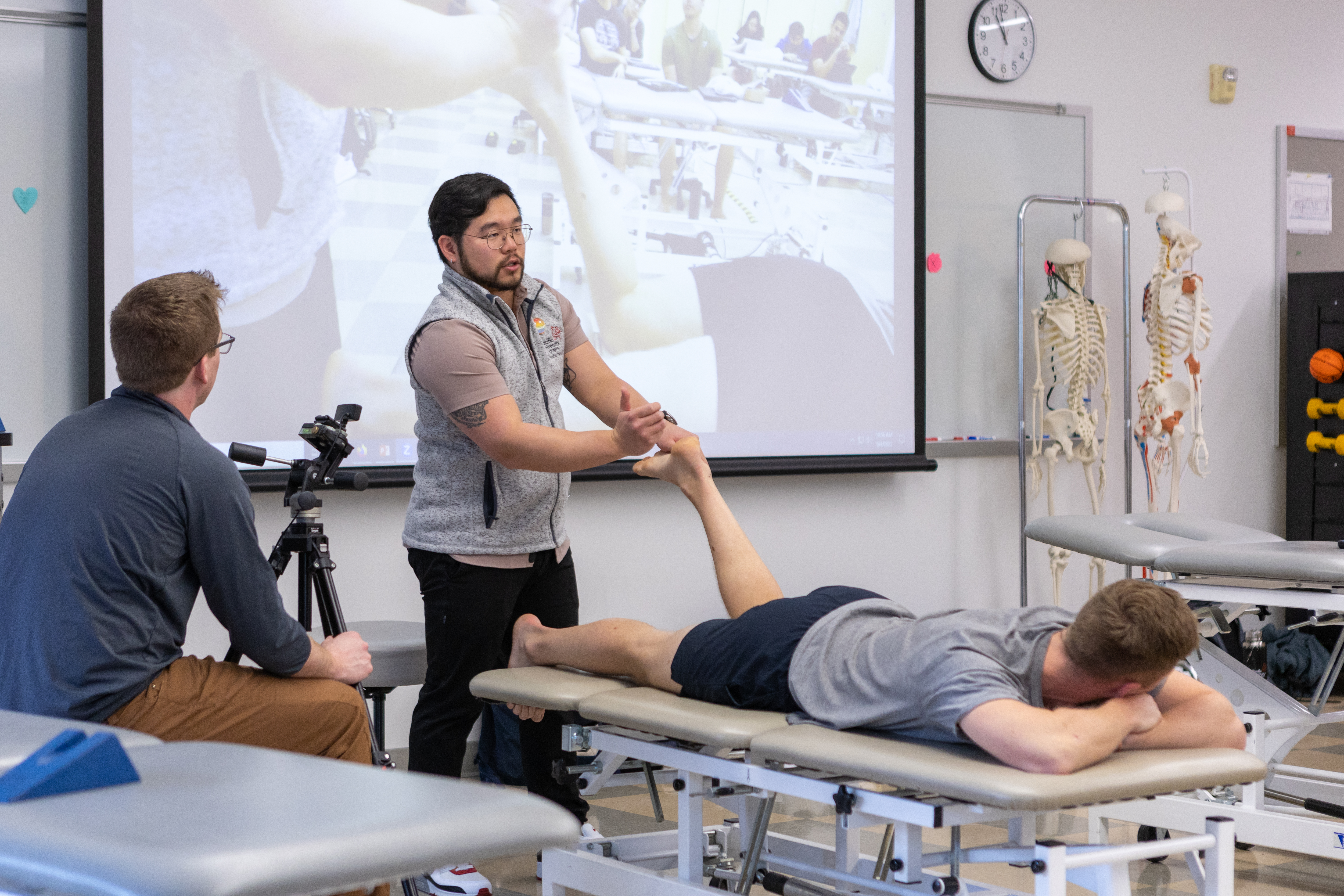 A physical therapy instructor demonstrates a way to strengthen the foot and leg on a student.