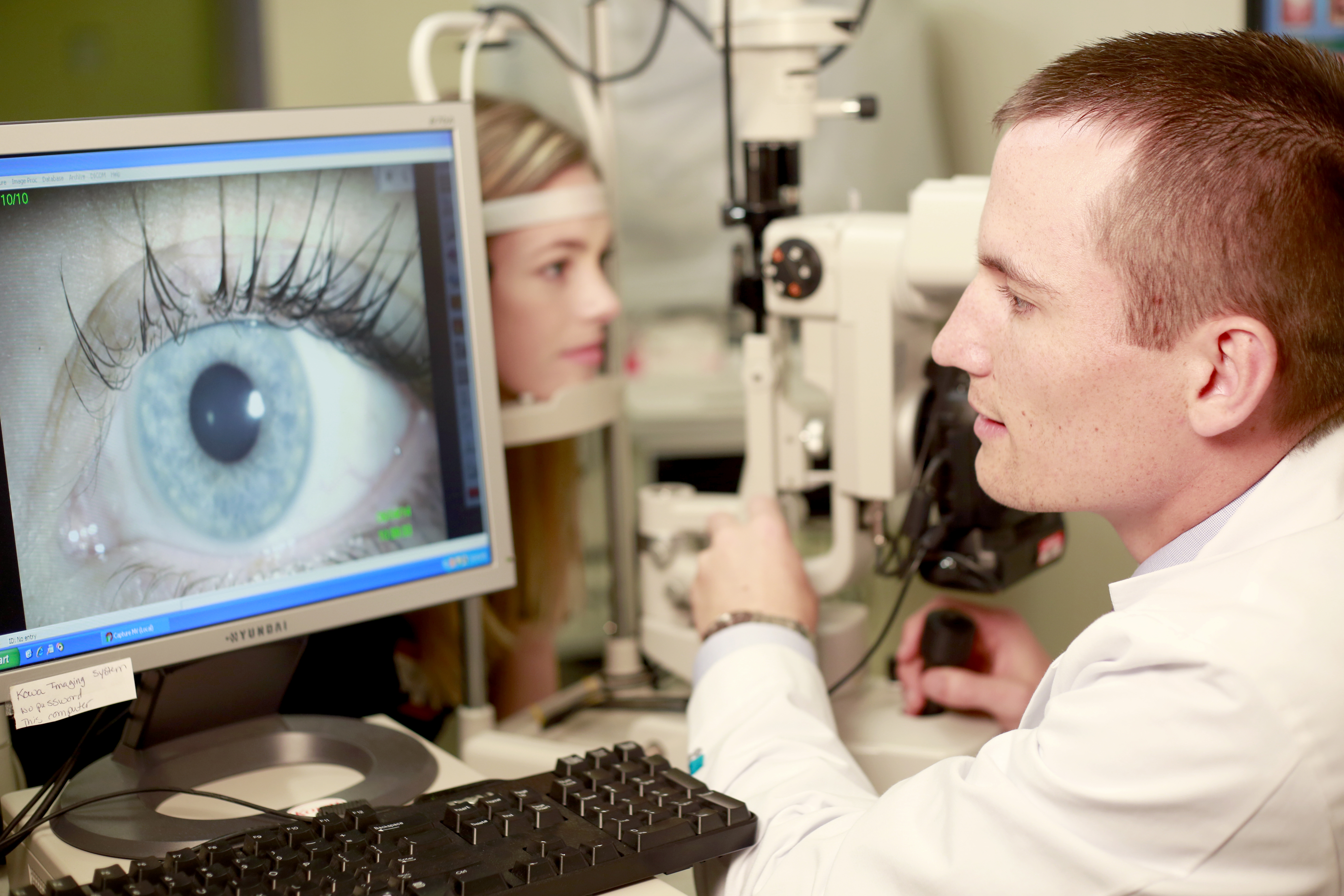 An optometry student examines a patient's eye using a large medical camera.