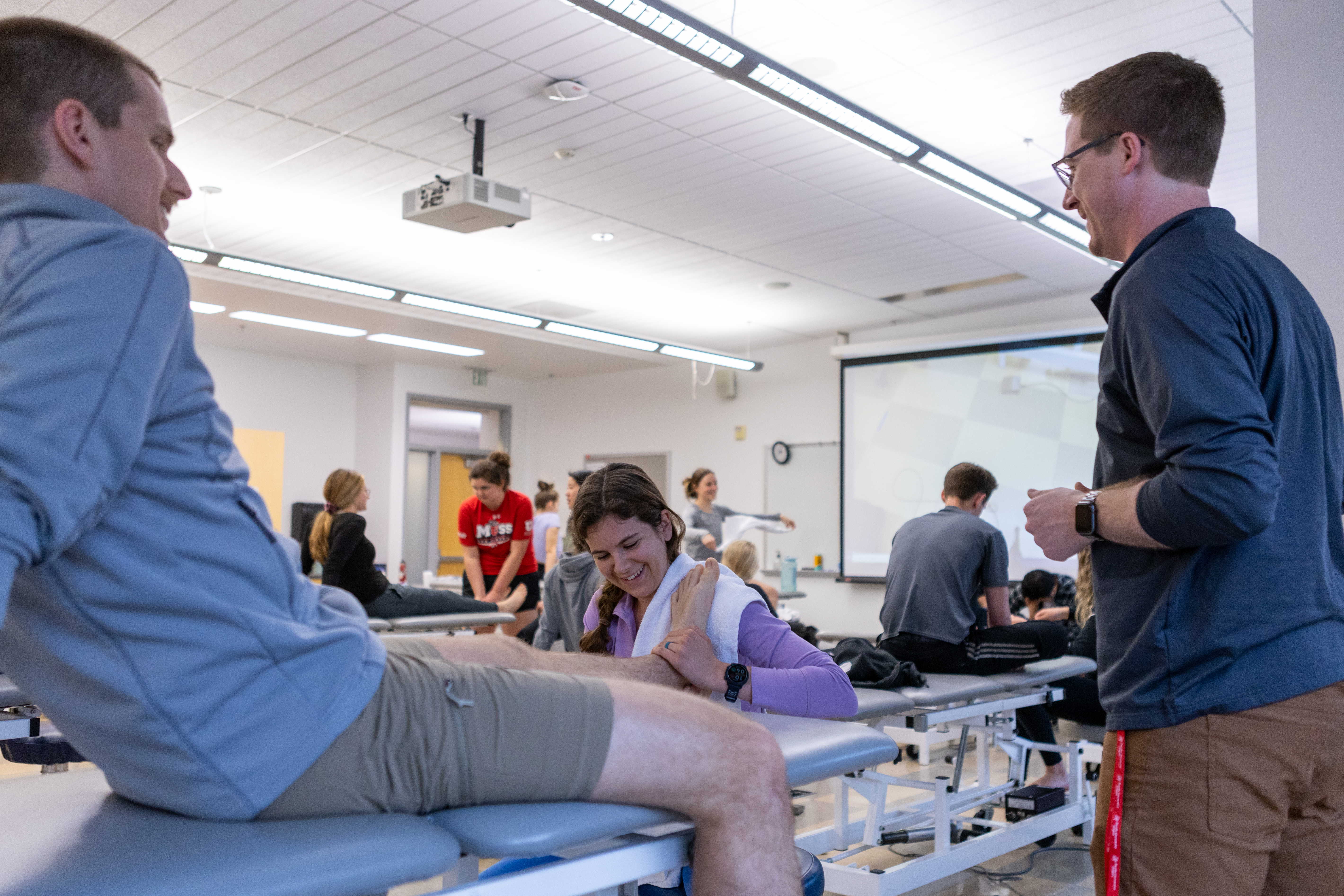 A physical therapy student learns a stretching exercise by demonstrating it on a patient.