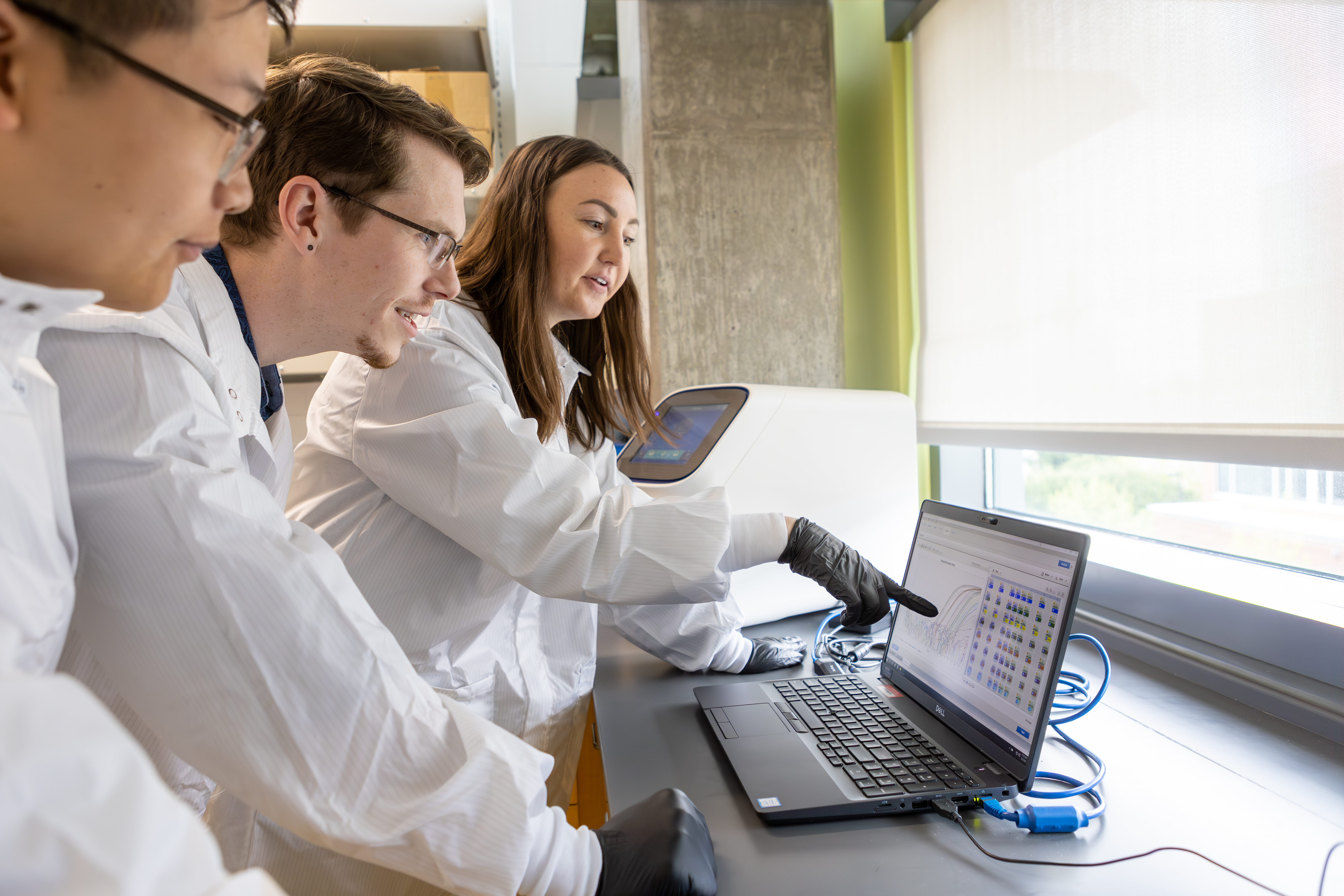 Three pharmacy students examine a computer screen in a medical lab. 