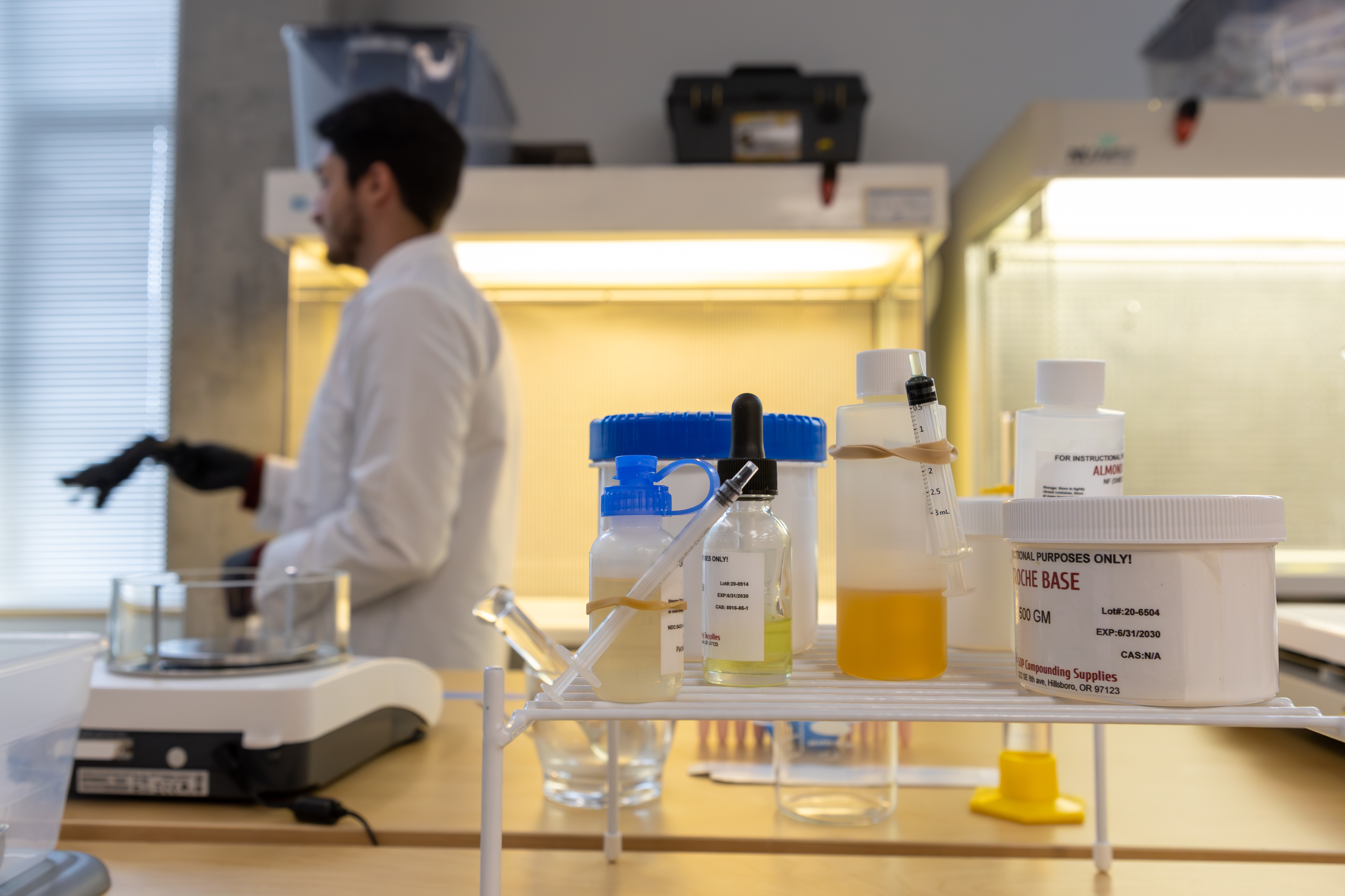A pharmacy student walks in the background while a set of pharmacy chemicals sits in the foreground. 