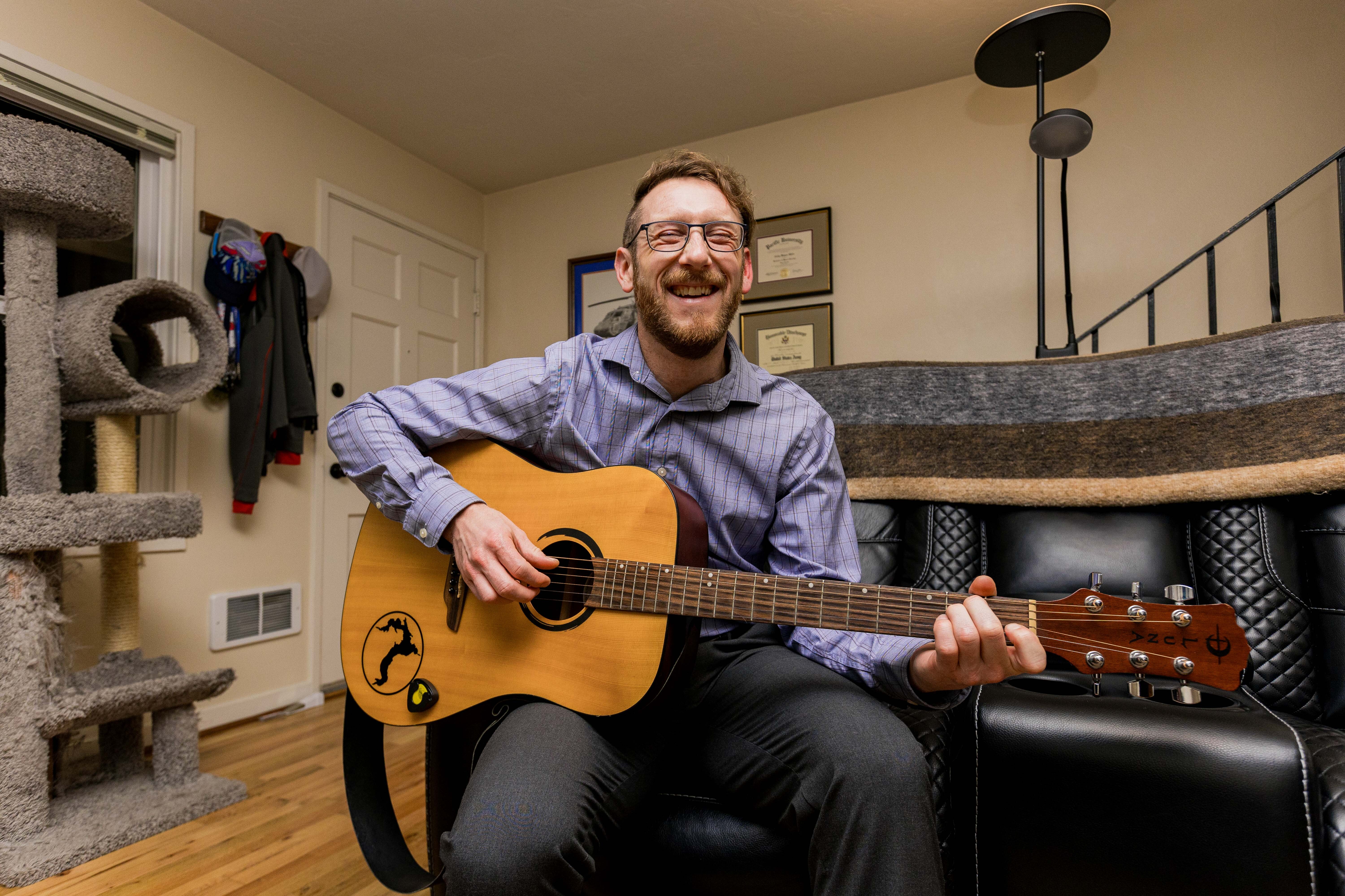 Alumni Cody Mills plays acoustic guitar in his home.