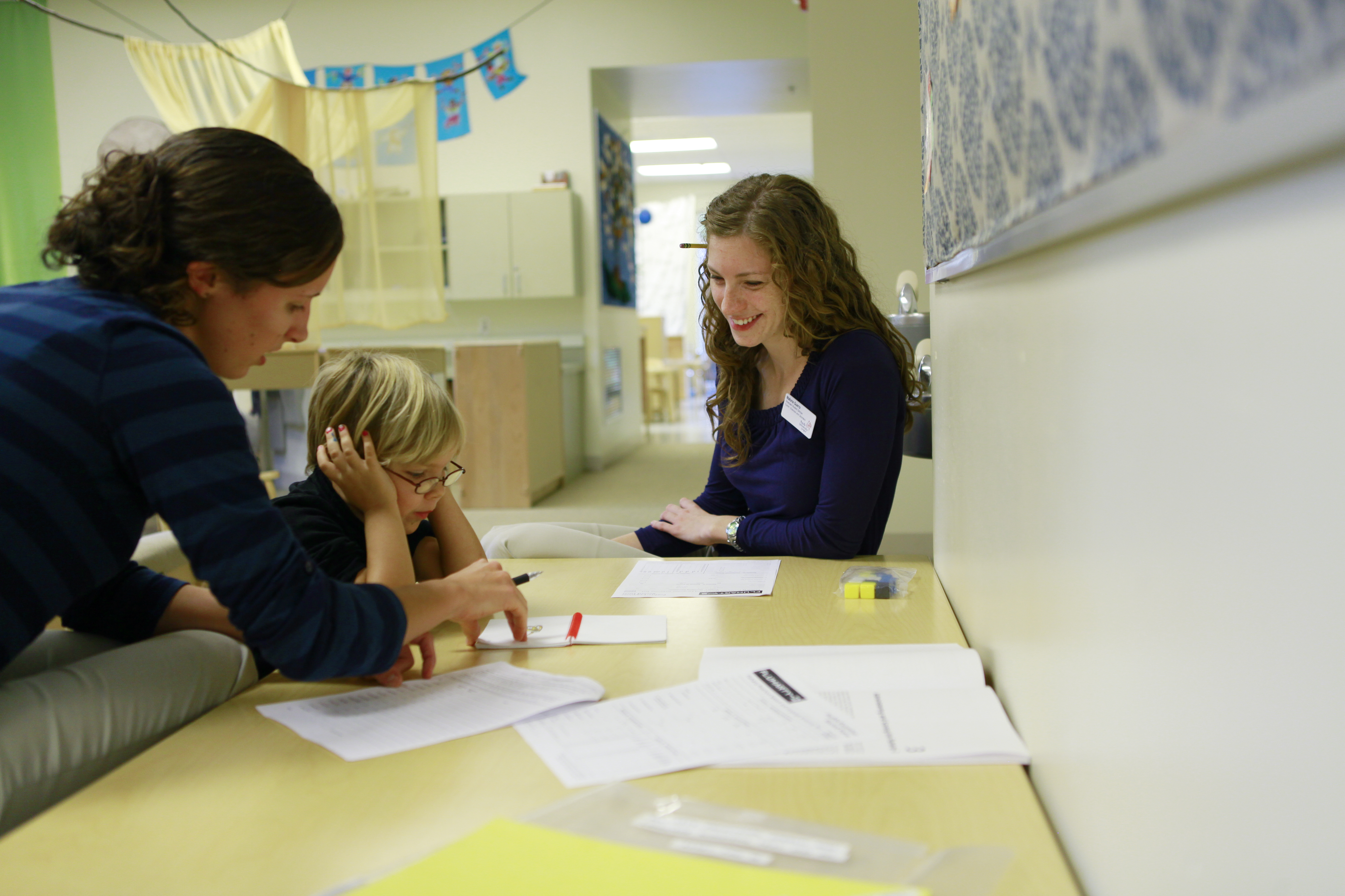 A speech therapy student works with a child and their adult in a speech pathology clinic.