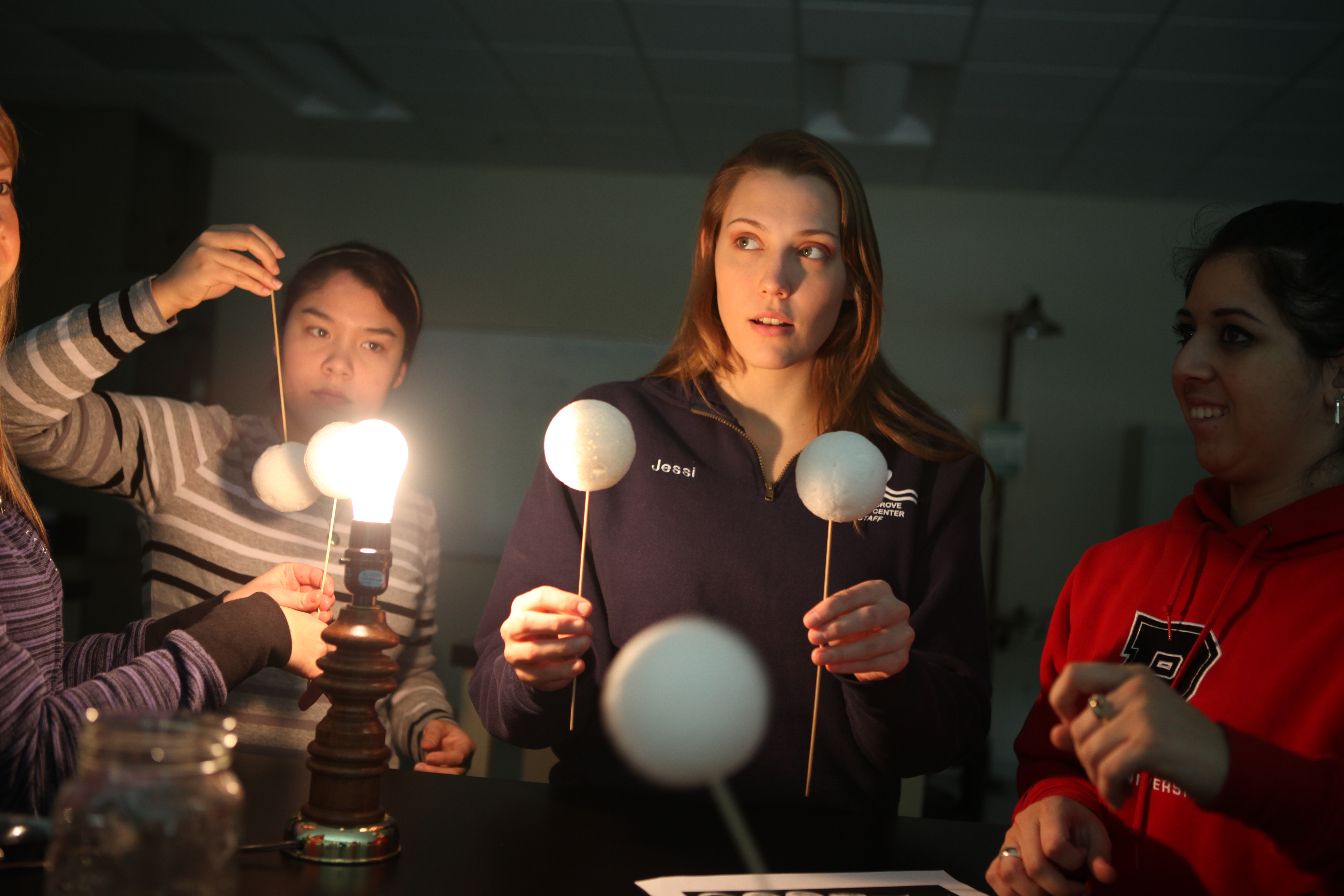 A female school teacher facilitates a demonstration model of the solar system for their students. 