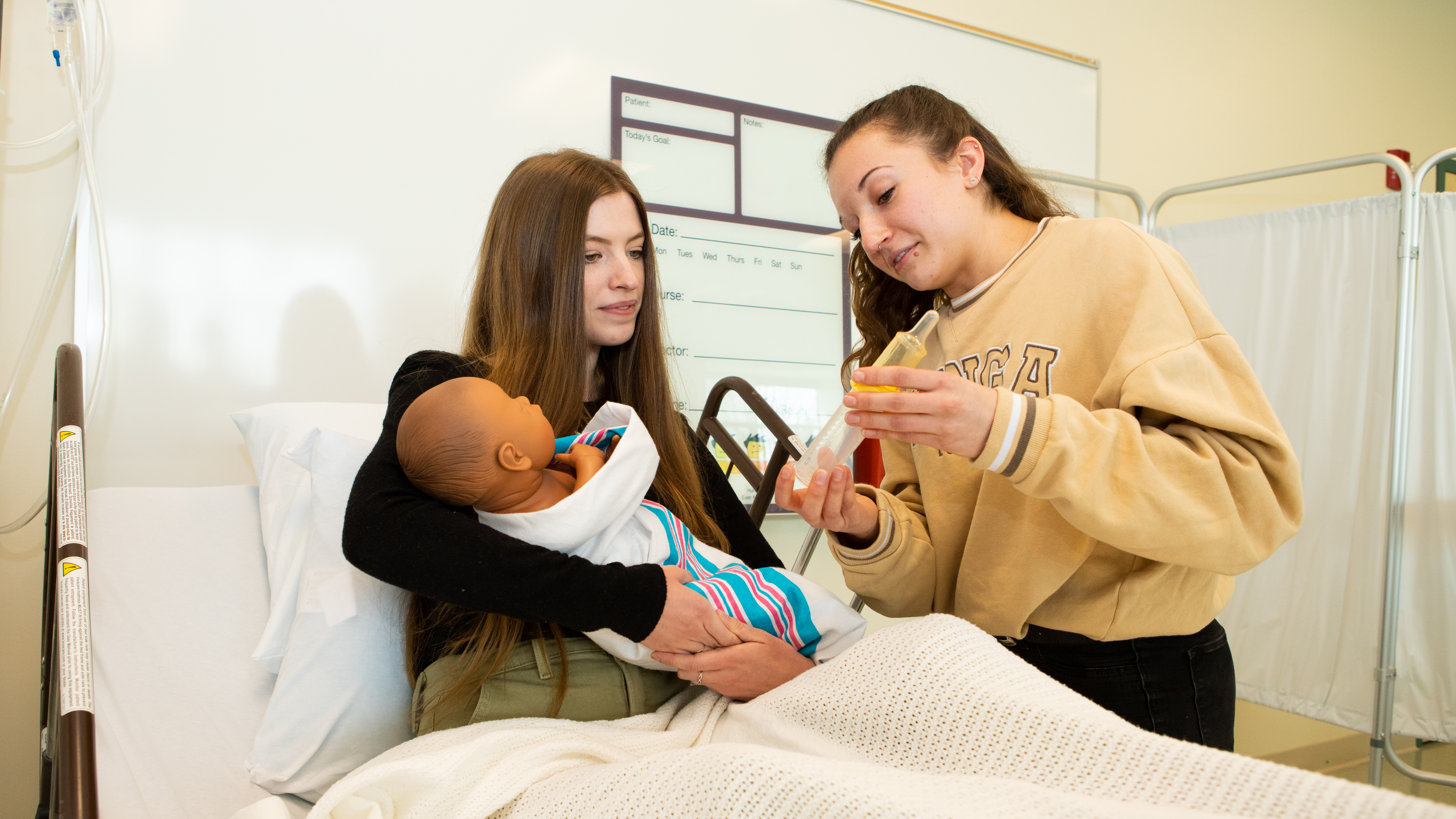 Two Pacific students demonstrate on a training dummy the best way to bottle-feed a baby.