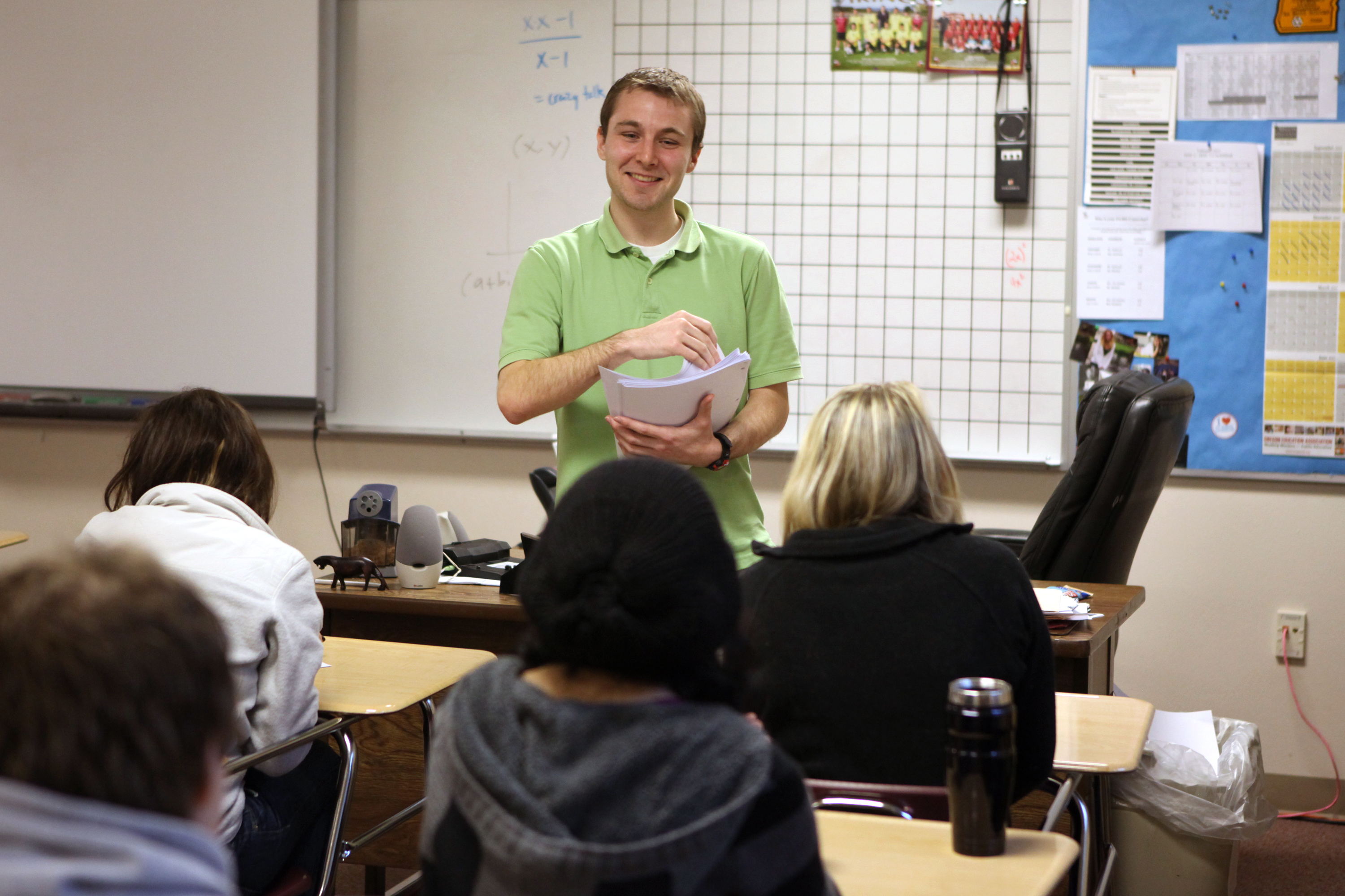 A student teacher hands papers out to a high school class.