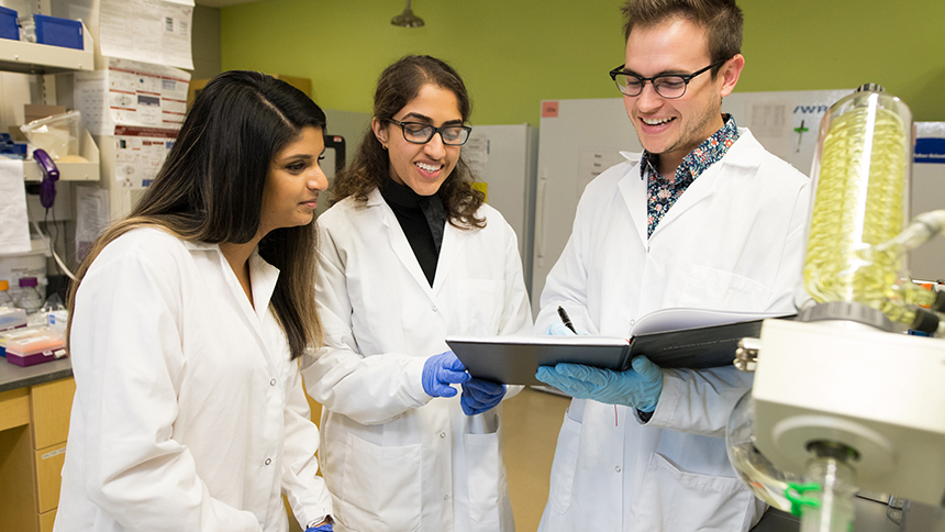 Three Pacific University students wearing white coats in the pharmacy lab