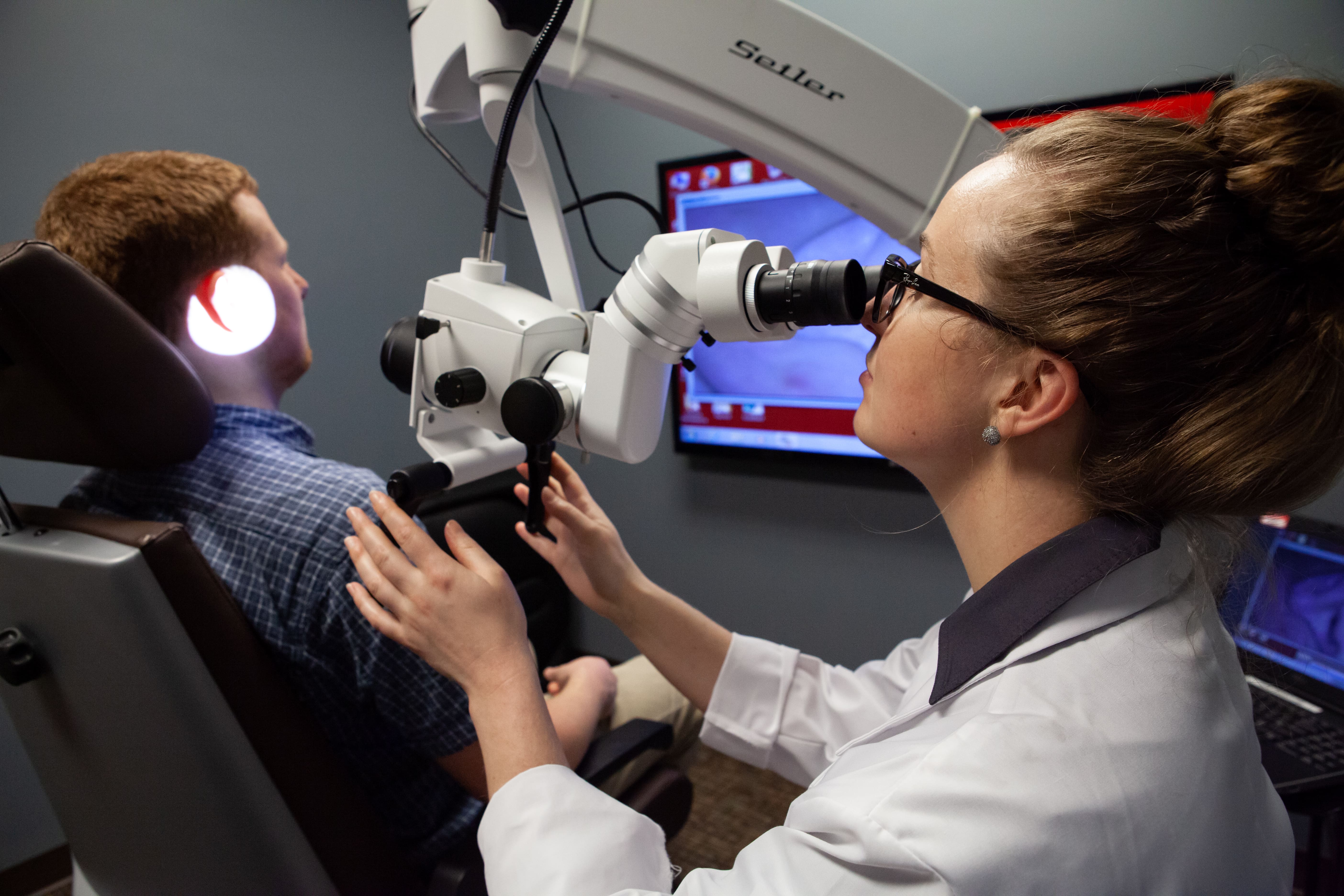 n audiology student examines a patient's ear using a medical camera.