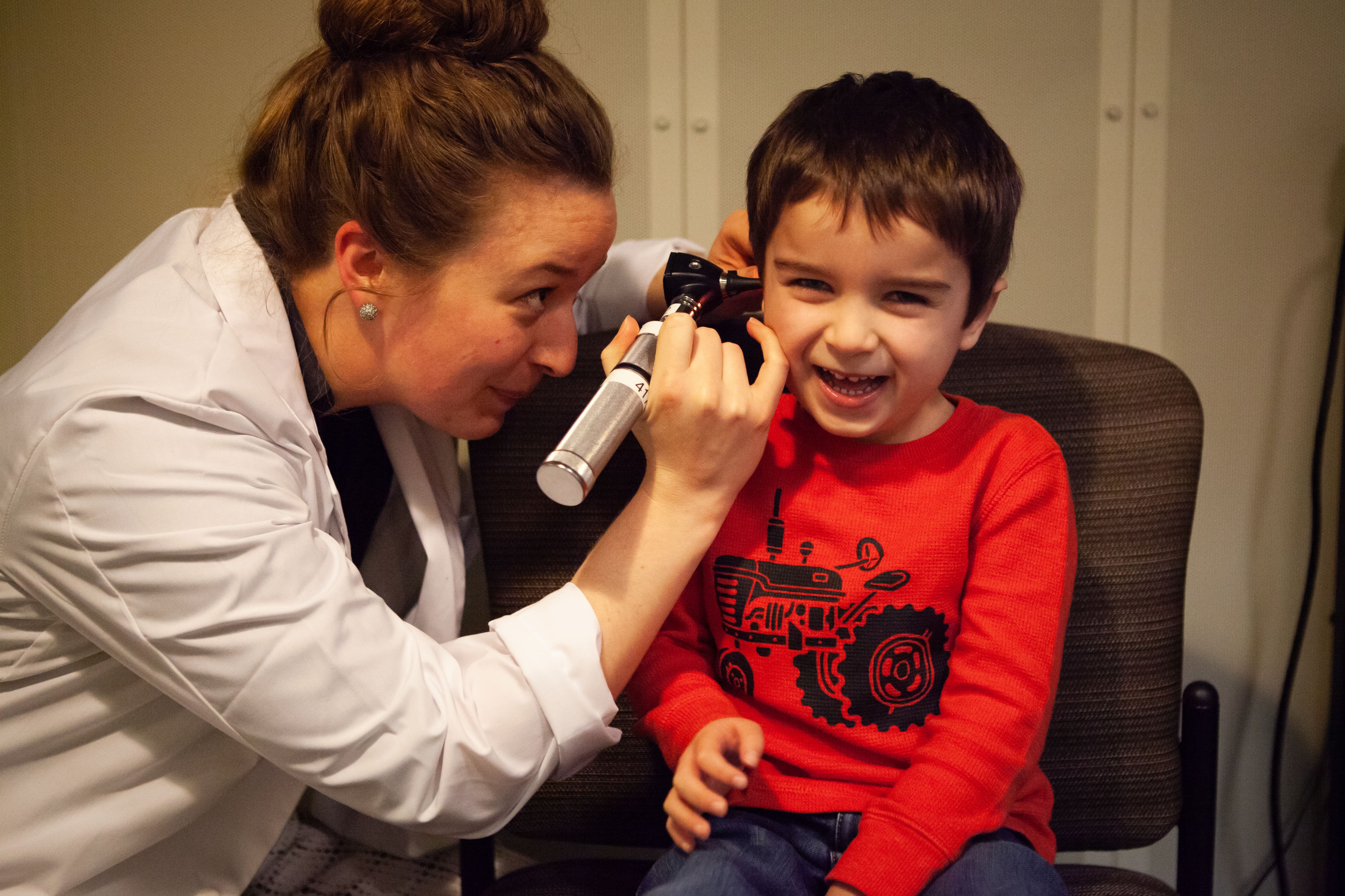 A Pacific audiology student uses an otoscope to look into a young child's ear.