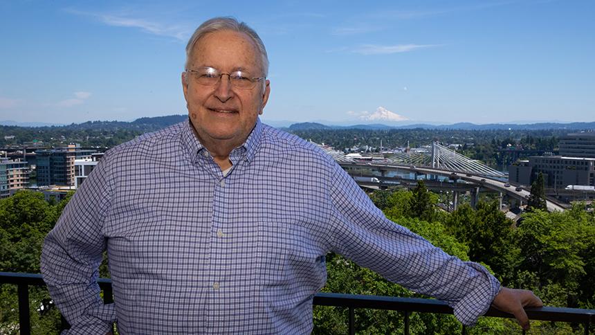 Les AuCoin stands in front of the Portland skyline with Mt Hood in the background