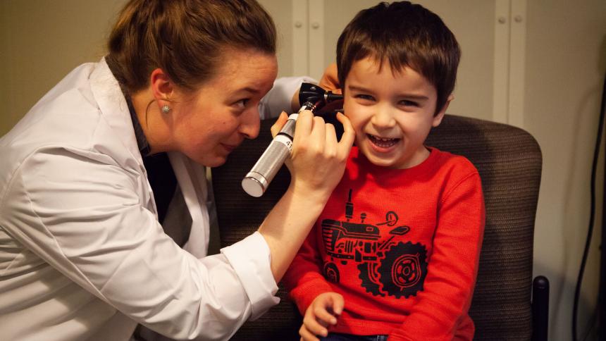 A Pacific audiology student uses an otoscope to look into a young child's ear.