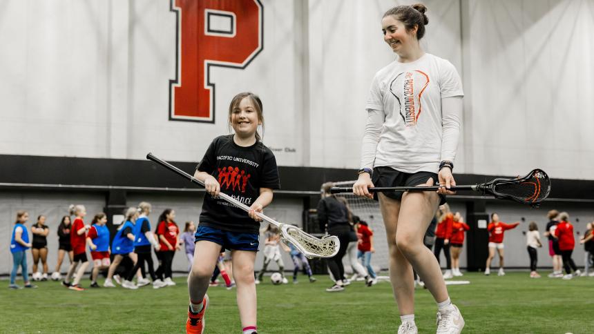 A woman teaches a young girl how to use a Lacrosse stick during the women and girls in sports event at Pacific's Stoller Center.