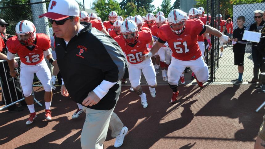 Photo of the Pacific University football team running to enter the field in 2014, led by then-coach Keith Buckley