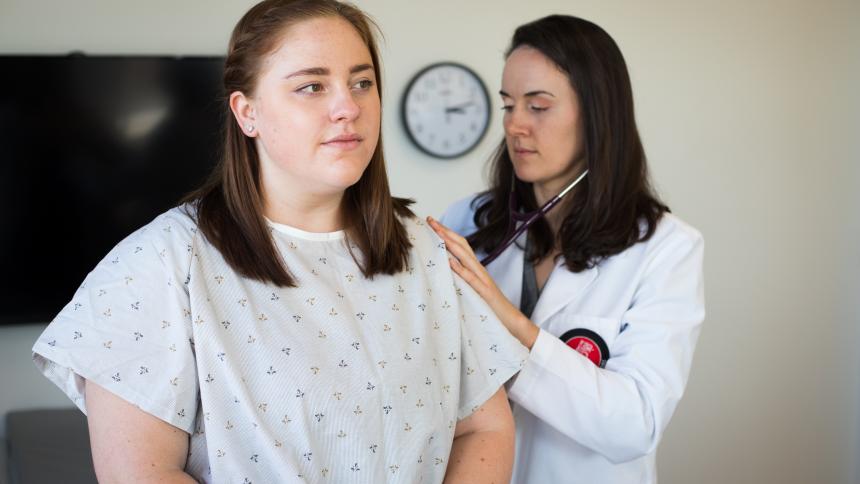 A physician assistant studies student listens to a patient's lungs using a stethoscope.