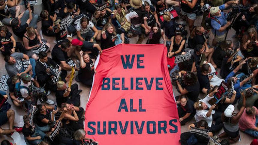 people holding a banner reading "we believe all survivors"