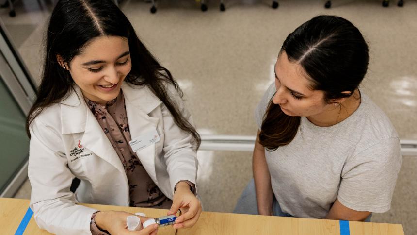 Two Pacific pharmacy students demonstrate how to explain medication instructions to patients.