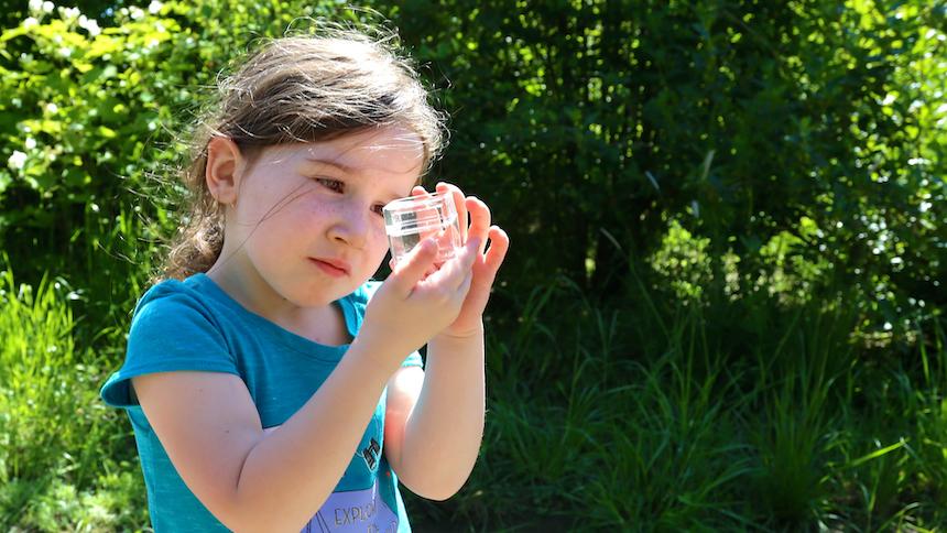 Girl looking into a glass jar in nature.