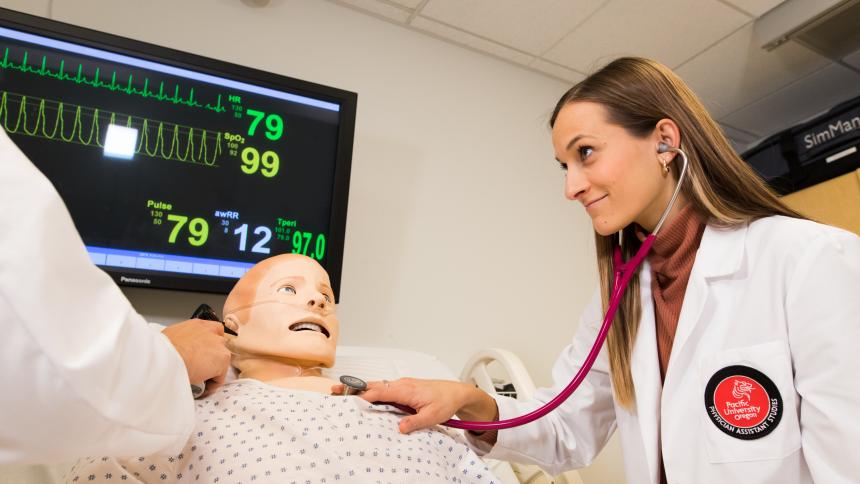 A physician assistant studies students practices using a stethoscope on a medical dummy.