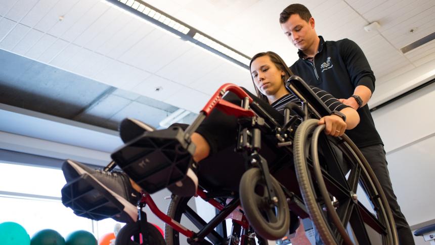 A physical therapy student demonstrates how to maneuver in a wheelchair with a patient.