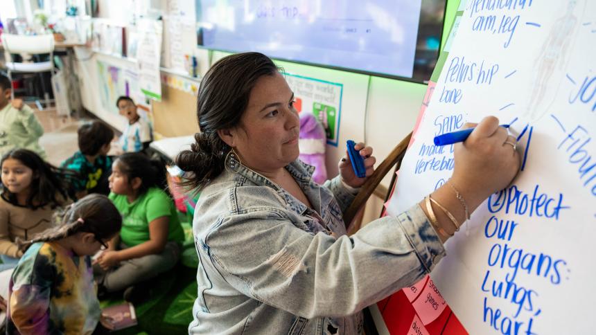 Pacific University alumna Kayla Davidson draws on a whiteboard in front of their elementary school students.