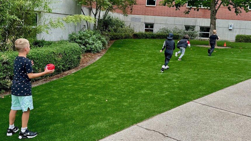 Child prepares to throw a football to three other children spread out on turf.