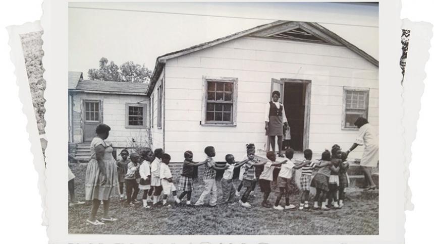 Young children walking out front of the school house. 