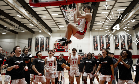 The men's basketball team celebrates as one player hangs from the rim