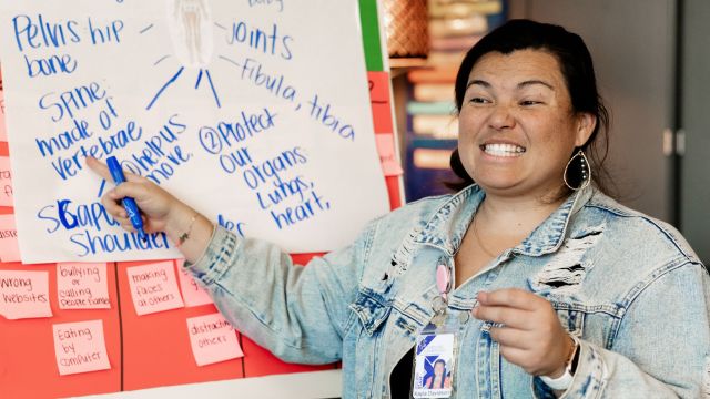 teacher smiling and pointing to a whiteboard