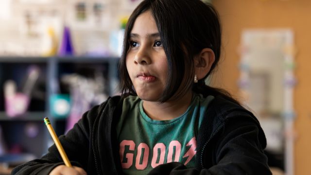 An elementary school student holds a pencil and thinks