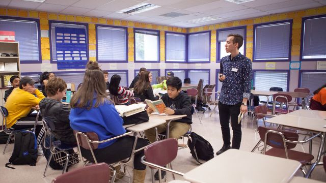 A Pacific University alumnus walks through a classroom of high school students