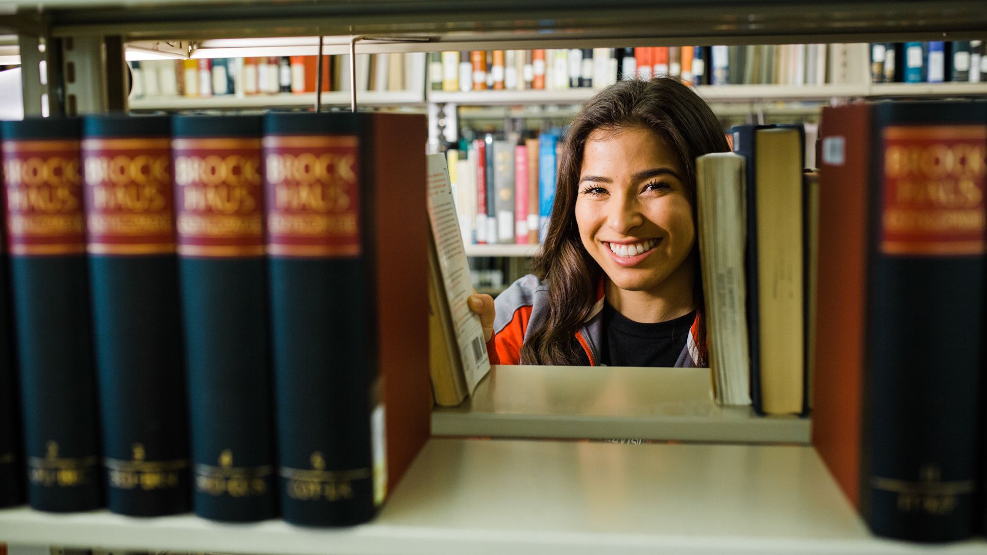 Student smiling, looking through shelf of books