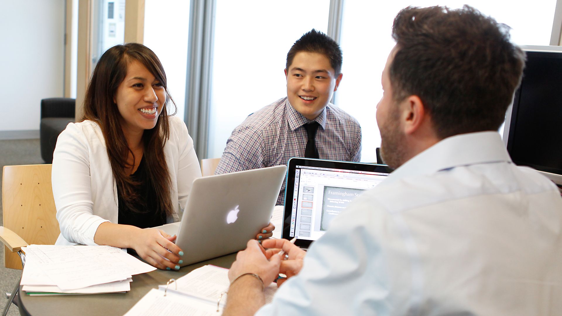 Three people at a table with laptops, talking